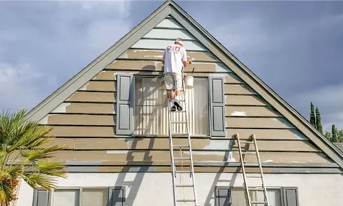 Painter working on the exterior siding of a house using a ladder