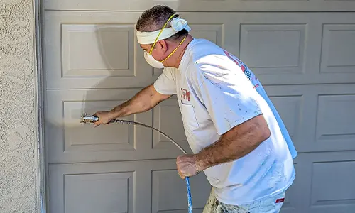 Garage door painting in progress using a spray gun by a professional painter