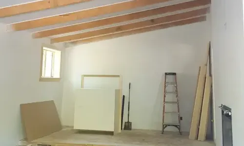 Interior painting in progress with exposed beams, ladder, and wall prep materials
